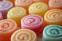 Colorful spiral jelly candy rolls covered in sugar crystals arranged in rows, showing vibrant pink, yellow, orange, and green sweet treats in macro view.