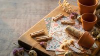Rustic gift wrapping setup with kraft paper, twine, dried flowers and terracotta pots on wooden surface for handmade present decoration ideas.