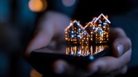Glowing miniature houses with warm lights reflecting on smartphone screen held in hands at night, creating magical bokeh effect and cozy atmosphere.