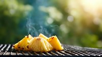 Grilled pineapple slices on barbecue grill with rising smoke and bokeh background, fresh tropical fruit cooking outdoors on summer day.