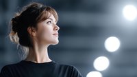 Young Caucasian woman in black top looking up with hope and determination against dramatic lighting background for motivation and inspiration concepts.