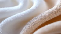 Soft white fabric waves creating gentle folds and curves in close-up macro photography, showcasing delicate textile texture and smooth flowing lines in neutral tones.