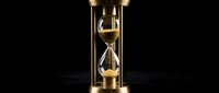 Brass hourglass with flowing golden sand against dark background, symbolizing time passage, deadline management, and temporal concepts for business and productivity applications.