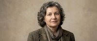Professional mature Hispanic businesswoman with curly gray hair in brown blazer smiling confidently against neutral background for corporate headshots.