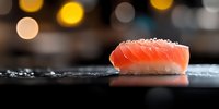 Fresh salmon nigiri sushi with rice and sea salt on black stone surface against blurred warm bokeh lights background, Japanese cuisine close-up.