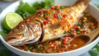 Grilled whole fish with spicy sauce, lime and herbs in white bowl. Fresh seafood dish with colorful vegetables and garnish for restaurant menu.
