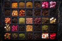 Colorful collection of dried flowers, spices, and tea ingredients in vintage wooden box compartments, creating vibrant culinary and aromatherapy composition on dark background.