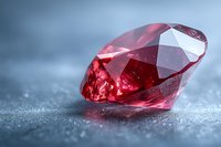Sparkling red ruby gemstone with brilliant cut facets on textured gray surface in macro photography, showcasing luxury jewelry and precious stone details.