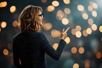 Young Caucasian woman in glasses and black sweater pointing up against blurred bokeh lights background, side view profile with warm evening atmosphere.