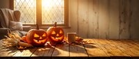 Halloween pumpkins with glowing faces on rustic wooden table in cozy autumn interior with warm sunlight streaming through window for seasonal decoration.