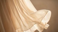 Flowing beige silk fabric with elegant drapes and soft folds creating luxurious textile movement for fashion and interior design projects.