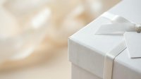 White gift box with silver ribbon on soft beige bokeh background for celebrations, holidays, birthdays, anniversaries, and special occasions.
