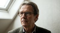 Senior Caucasian businessman with glasses in contemplative pose wearing brown sweater in modern office with natural lighting for corporate presentations.
