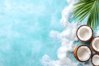 Fresh coconut halves with palm leaf on turquoise blue background with white foam texture, creating tropical summer beach atmosphere. Perfect for food and beverage designs.