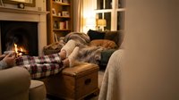 Cozy evening at home with person relaxing on sofa by fireplace in warm living room with built-in shelves and soft lighting for comfort and relaxation.