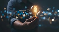 Businessman holding glowing lightbulb with innovation and ideas text against bokeh background representing creativity and business solutions.