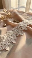 Delicate ivory lace trim with rose motifs arranged on soft beige fabric with dried flowers and pearl beads, ideal for wedding invitations and bridal design projects.