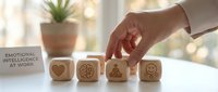 Professional woman hand arranging wooden blocks with emotional intelligence symbols on modern office desk for workplace development and team building.