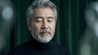 Mature businessman with gray hair and beard in black turtleneck with closed eyes in contemplative pose against blurred background for corporate content.