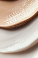 Smooth beige and white cream texture with gentle swirls creating an elegant abstract background pattern, suitable for cosmetic and skincare product marketing.