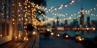Romantic evening on wooden terrace with string lights and lantern overlooking blurred city skyline at twilight.