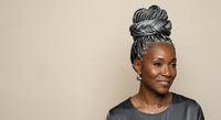 African American woman with gray braided updo hairstyle wearing black shirt against neutral background, suitable for beauty, fashion, and lifestyle editorial use.
