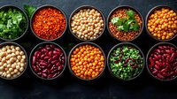 Colorful variety of legumes, pulses and herbs in black bowls arranged in rows on dark background, fresh ingredients for healthy cooking and protein source.