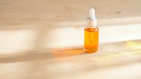 Amber glass dropper bottle with golden serum on wooden surface with warm sunlight creating natural shadows for skincare and cosmetic products.