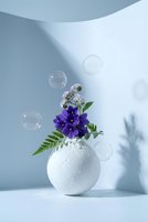 White ceramic vase with purple flowers and green ferns surrounded by floating soap bubbles on clean minimalist background for home decor and wellness concepts.