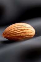 Single fresh almond macro shot on dark background with soft lighting showing natural texture and ridges of nut shell, suitable for food photography and packaging.