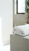 Rolled white towel on concrete pedestal in minimalist bathroom with natural light, potted plant, and window for spa, hotel, and wellness design projects.