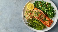Grilled salmon fillet served with quinoa, fresh kale salad and asparagus on white plate. Healthy mediterranean meal with herbs, lemon and vegetables.