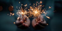 Hands holding bright sparklers creating magical golden sparks and light trails against dark background for celebration and festive occasions.