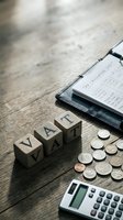 VAT wooden letter blocks with calculator, coins and invoice on rustic desk for tax accounting and business finance concepts.