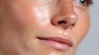Close-up of glowing skin with natural pores, dewy complexion, and soft pink lips against neutral background, showcasing skincare results.