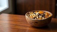 Wooden bowl filled with mixed nuts and dried fruits on rustic table for healthy snacking and cooking ingredients.