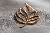 Delicate golden maple leaf brooch on gray linen textile background with soft focus. Vintage style jewelry detail showcasing intricate metalwork pattern and texture.