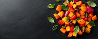 Fresh diced butternut squash with vibrant basil leaves scattered on dark slate background, raw organic produce for cooking seasonal autumn dishes.