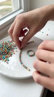 Close-up of hands stringing colorful beads onto wire to create handmade jewelry bracelets. Craft hobby and DIY beadwork project for creative leisure activities and artisan accessory making.