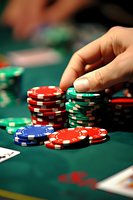 Stacks of colorful poker chips on green felt table with player's hand placing bet, capturing intense gaming atmosphere in casino setting. Suitable for gambling articles.
