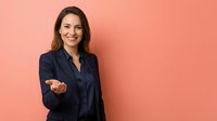 Professional businesswoman in navy blazer extending welcoming hand gesture against coral background for corporate presentations and marketing materials.