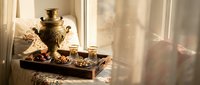Traditional Russian samovar with tea glasses and sweets on wooden tray in warm sunlit interior for authentic cultural dining experience.