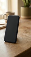 Black smartphone leaning on wooden desk in cozy home office workspace with coffee mug and plant creating warm productive atmosphere for remote work and communication.