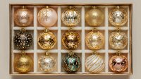 Luxurious collection of elegant Christmas ornaments in gold, rose gold, and silver tones arranged in a display box, perfect for holiday decorating.