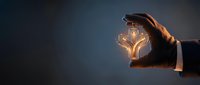 Businessman hands protecting glowing lightbulb with book pages inside symbolizing knowledge protection and educational innovation concept.