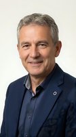 Portrait of mature man with gray hair wearing navy blazer and dark shirt, smiling at camera against neutral background for corporate and professional use.