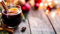 Festive mulled wine with orange slice, cinnamon sticks and star anise on rustic wooden table. Christmas lights and decorations create cozy atmosphere.