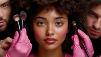 Young African American woman with natural curly hair surrounded by makeup artists wearing pink gloves holding professional makeup brushes near her face.