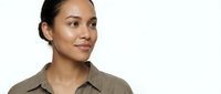 Young mixed-race businesswoman in beige shirt smiling confidently against white background for corporate headshot and professional marketing materials.