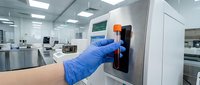 Laboratory technician in blue gloves operating modern medical equipment in sterile clinical environment for scientific research and diagnostics.
